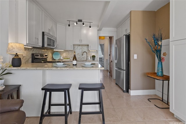 kitchen featuring a peninsula, stainless steel appliances, decorative backsplash, and white cabinets