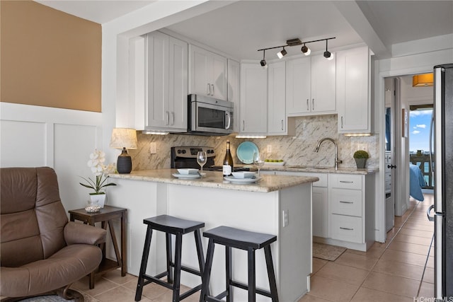 kitchen featuring a peninsula, light tile patterned floors, a kitchen bar, a sink, and appliances with stainless steel finishes
