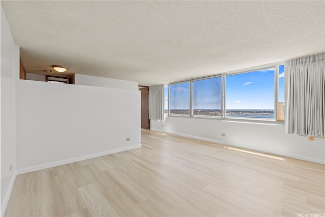 unfurnished room with baseboards, a textured ceiling, and light wood-style flooring