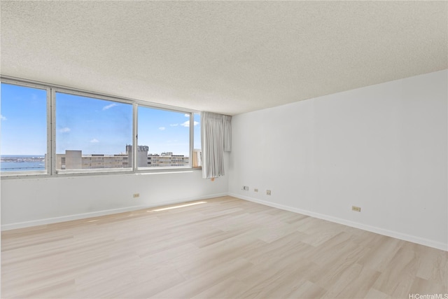 empty room featuring light wood-style floors, baseboards, and a textured ceiling