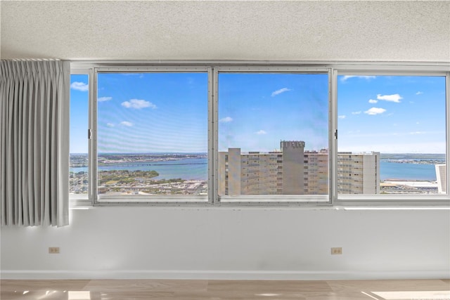 empty room featuring a water view, baseboards, wood finished floors, and a textured ceiling