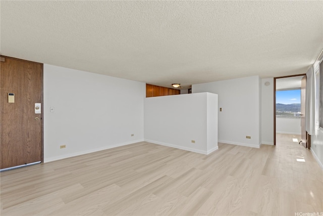 spare room featuring light wood-style floors, a textured ceiling, and baseboards