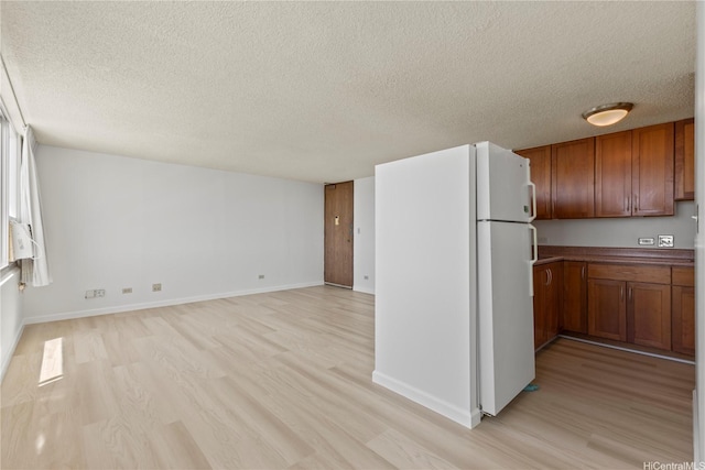 kitchen with light wood-type flooring, freestanding refrigerator, brown cabinetry, and a textured ceiling