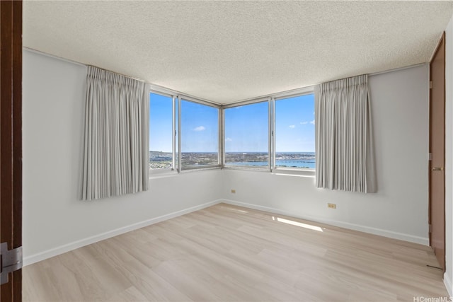 unfurnished room with a water view, baseboards, light wood-type flooring, and a textured ceiling