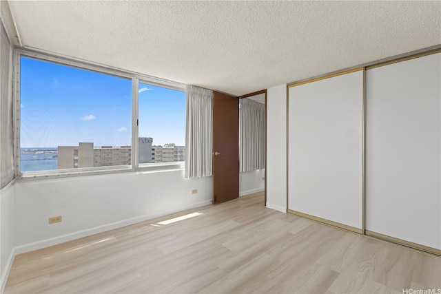 unfurnished bedroom with baseboards, a textured ceiling, wood finished floors, and a closet
