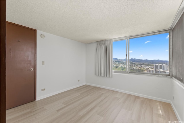 unfurnished room featuring baseboards, light wood finished floors, a mountain view, and a textured ceiling
