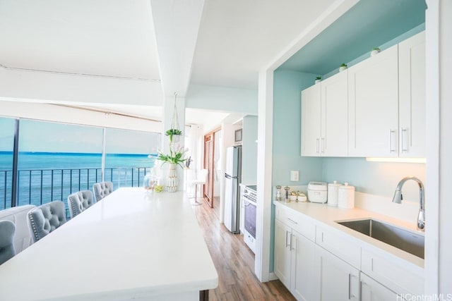 kitchen featuring a sink, light wood-style floors, freestanding refrigerator, white cabinetry, and a water view