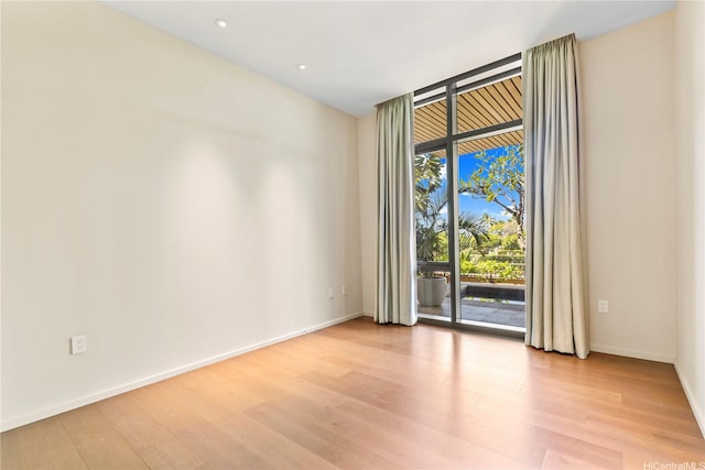 empty room featuring baseboards, recessed lighting, light wood finished floors, and floor to ceiling windows