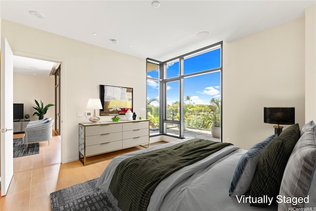 bedroom featuring expansive windows, light wood-style flooring, and access to exterior