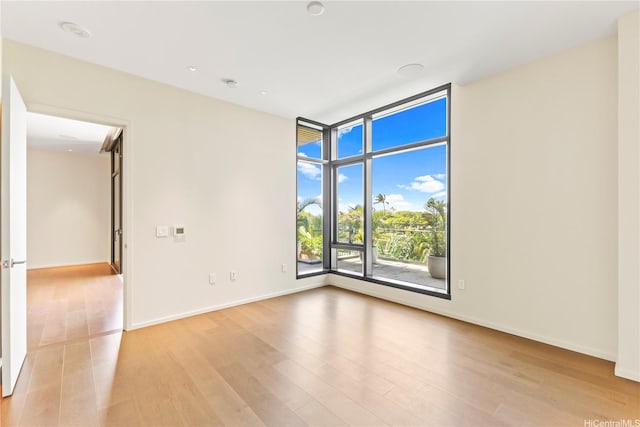 spare room featuring expansive windows, baseboards, and wood finished floors