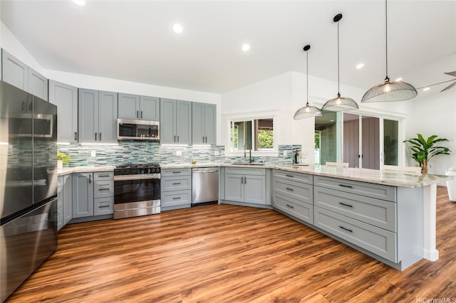 kitchen featuring appliances with stainless steel finishes, a sink, a peninsula, backsplash, and gray cabinetry
