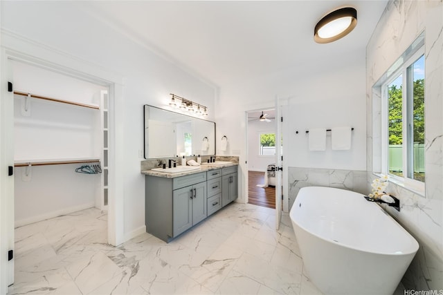 bathroom with double vanity, marble finish floor, a walk in closet, a freestanding bath, and a sink