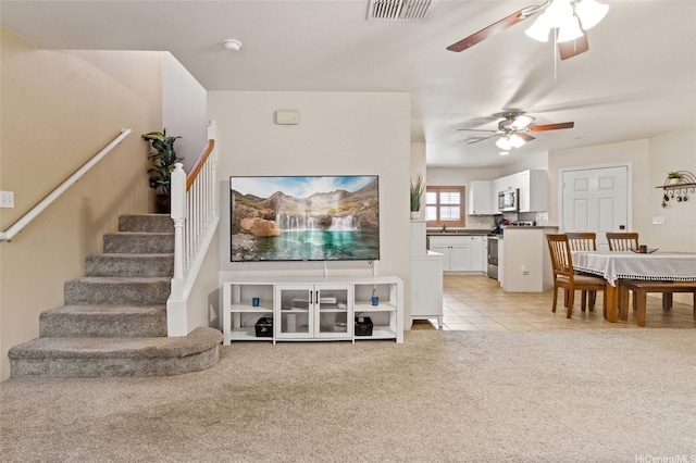 living area featuring a ceiling fan, light colored carpet, visible vents, stairway, and light tile patterned floors