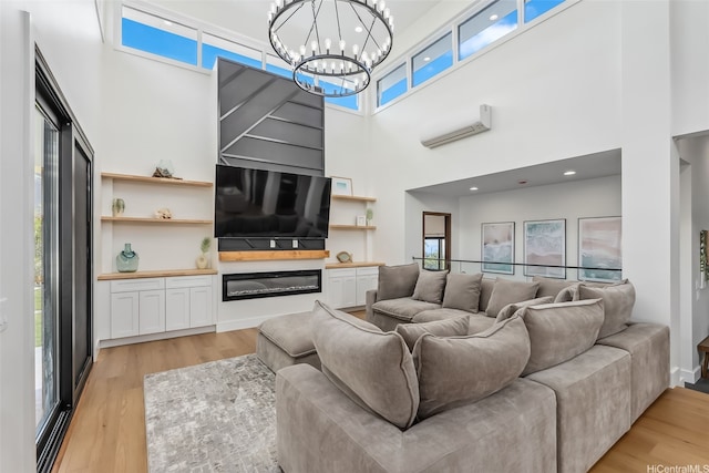 living room featuring a wall unit AC, a notable chandelier, light wood-type flooring, and a towering ceiling