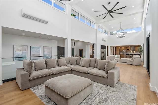 living area featuring an inviting chandelier, an AC wall unit, light wood-style flooring, recessed lighting, and a towering ceiling