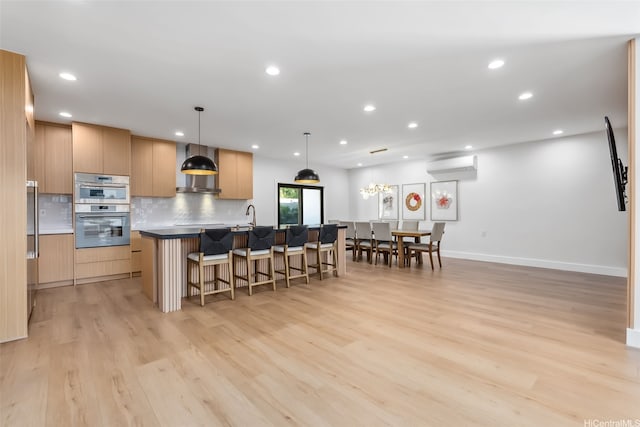 kitchen featuring a kitchen island with sink, a breakfast bar area, an AC wall unit, stainless steel double oven, and light wood finished floors