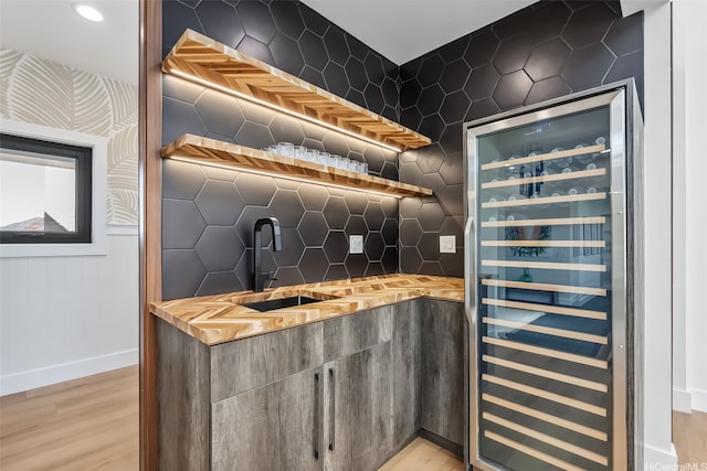 bar with light wood-style floors, beverage cooler, indoor wet bar, baseboards, and tasteful backsplash