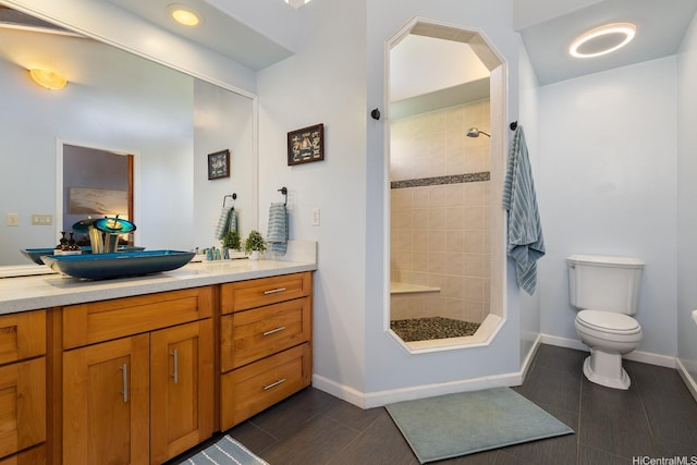 bathroom featuring vanity, baseboards, toilet, and tiled shower
