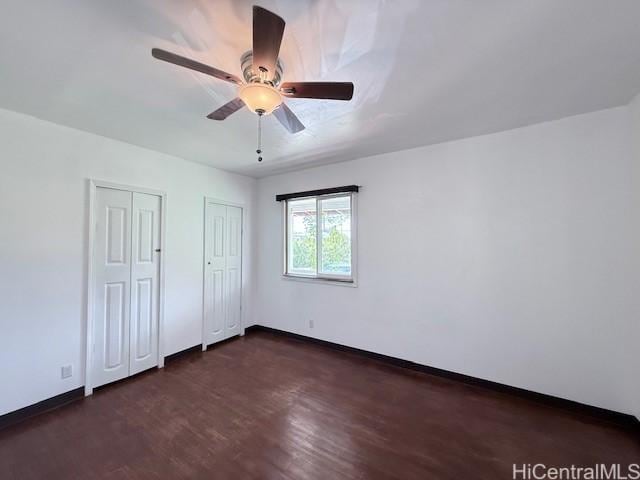 unfurnished bedroom featuring baseboards, a ceiling fan, multiple closets, and wood finished floors