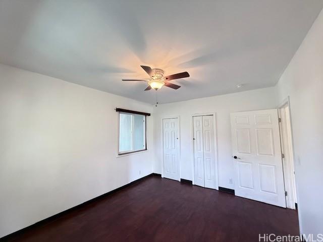 unfurnished bedroom featuring ceiling fan, dark wood-style flooring, baseboards, and multiple closets