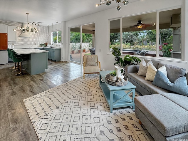 living room featuring ceiling fan with notable chandelier and light wood-style flooring