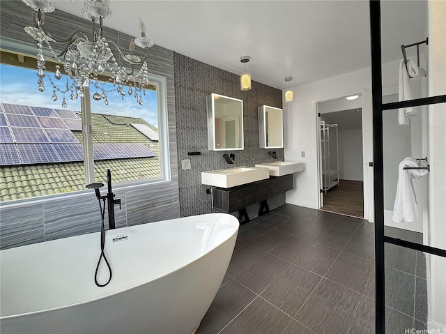 full bathroom with an inviting chandelier, double vanity, a freestanding tub, tile patterned floors, and a sink