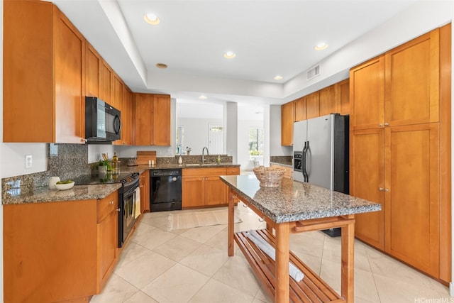 kitchen featuring visible vents, brown cabinets, a sink, black appliances, and dark stone counters