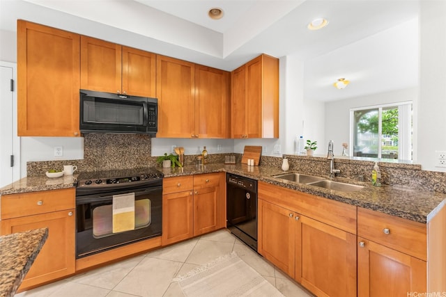 kitchen featuring brown cabinetry, a sink, dark stone counters, and black appliances