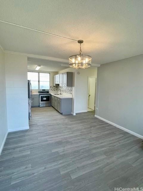 kitchen with a textured ceiling, appliances with stainless steel finishes, a sink, baseboards, and an inviting chandelier