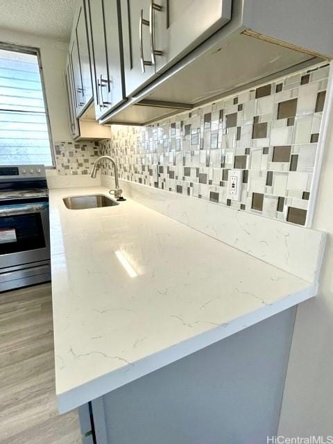 kitchen featuring electric range, light stone countertops, a sink, light wood-style flooring, and backsplash