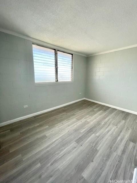 empty room with concrete block wall, a textured ceiling, ornamental molding, and wood finished floors