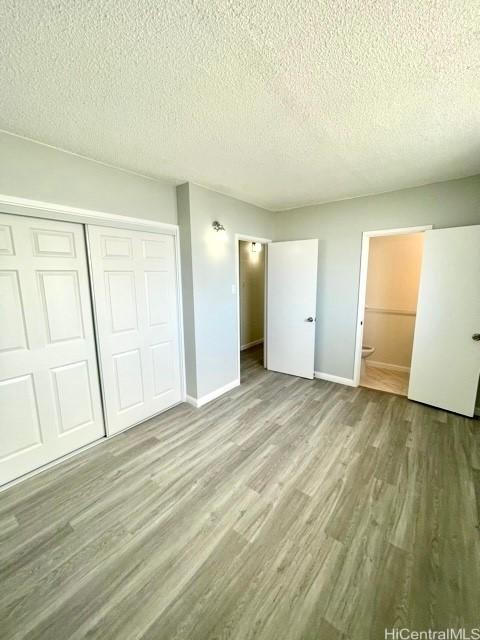 unfurnished bedroom featuring a textured ceiling, baseboards, a closet, and wood finished floors