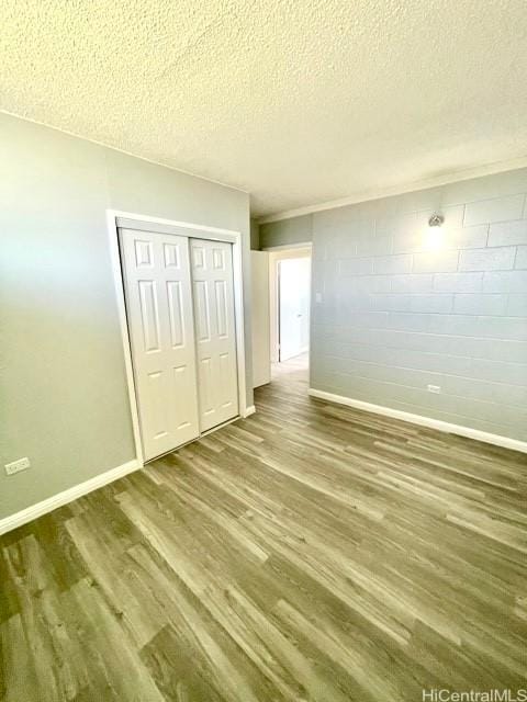 unfurnished bedroom featuring a closet, wood finished floors, baseboards, a textured ceiling, and concrete block wall