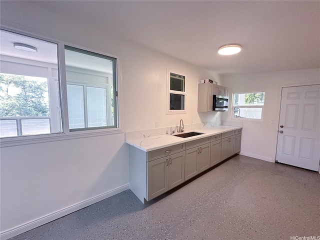 kitchen with gray cabinetry, stainless steel microwave, baseboards, and a sink