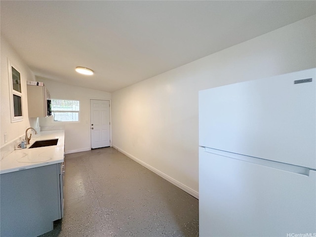 kitchen featuring finished concrete floors, a sink, freestanding refrigerator, baseboards, and light stone counters