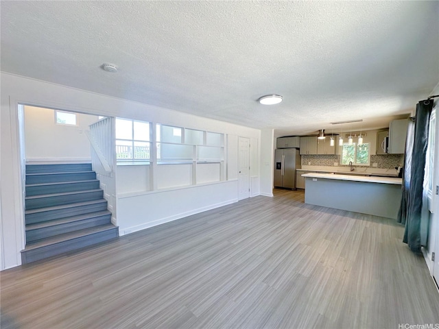 unfurnished living room with baseboards, stairway, light wood-type flooring, and a textured ceiling