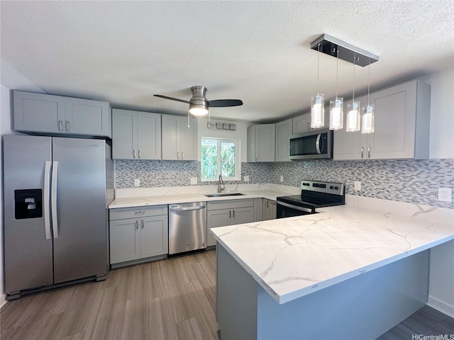 kitchen with stainless steel appliances, a peninsula, a sink, and gray cabinets