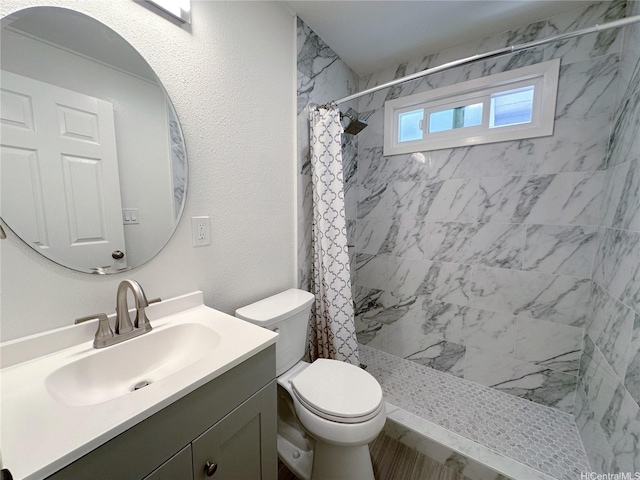 full bath featuring toilet, tiled shower, and vanity