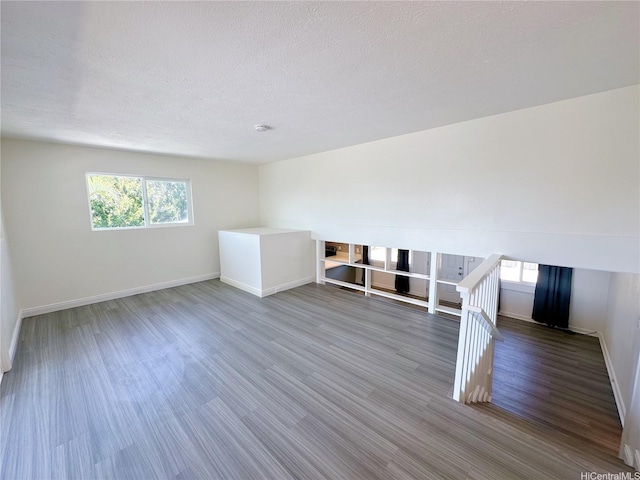 unfurnished living room featuring a textured ceiling, baseboards, and wood finished floors