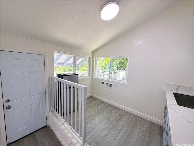 staircase with wood finished floors, vaulted ceiling, baseboards, and ornamental molding
