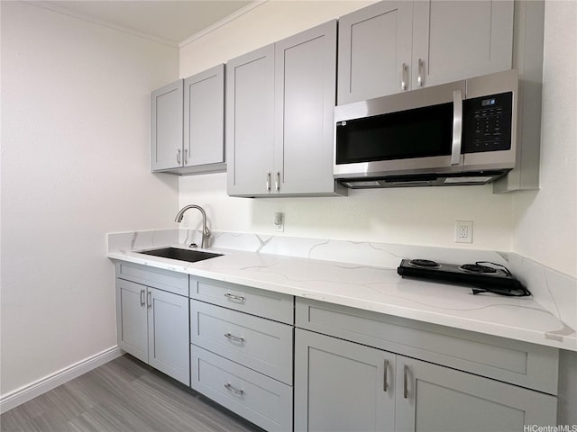 kitchen featuring light wood finished floors, a sink, stainless steel microwave, light stone countertops, and gray cabinetry