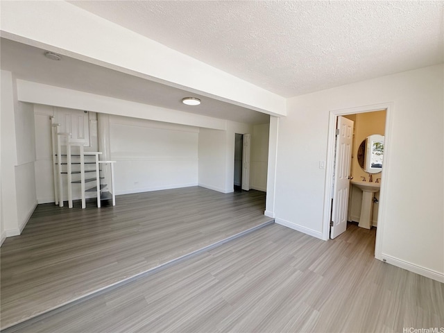 unfurnished room featuring a sink, light wood-style flooring, a textured ceiling, and baseboards