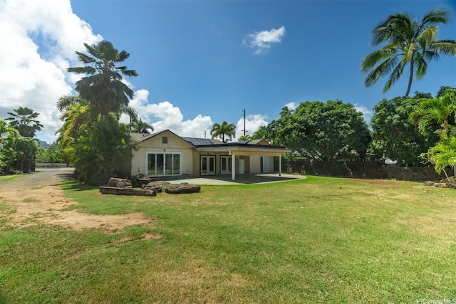 back of house featuring a lawn, french doors, fence, a patio, and roof mounted solar panels