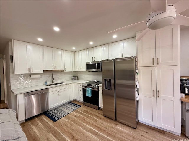 kitchen featuring a sink, stainless steel appliances, white cabinetry, light countertops, and backsplash