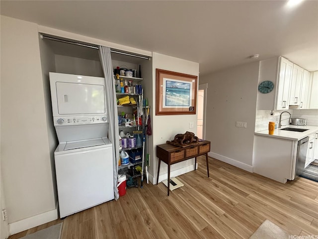 washroom featuring a sink, laundry area, stacked washer and dryer, baseboards, and light wood-style floors