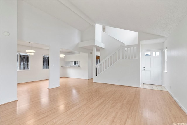 unfurnished living room featuring stairs, light wood finished floors, high vaulted ceiling, and baseboards