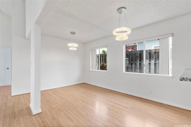 unfurnished dining area with wood finished floors, a textured ceiling, a chandelier, and baseboards