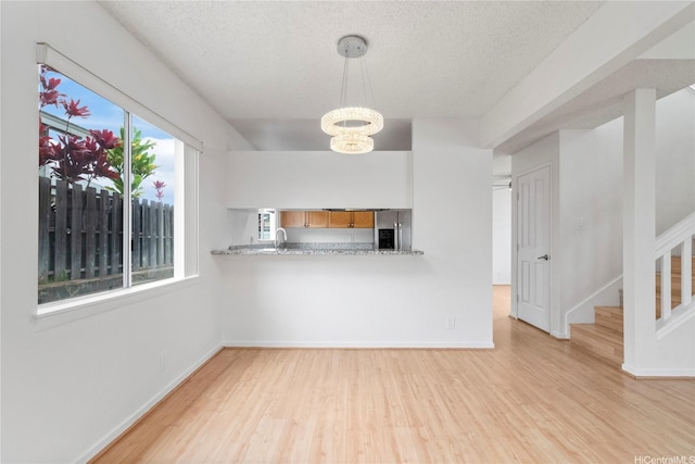 unfurnished living room featuring light wood-style floors, a chandelier, a textured ceiling, stairway, and baseboards