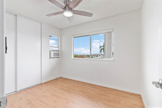 unfurnished bedroom featuring light wood finished floors, a textured ceiling, cooling unit, a closet, and baseboards