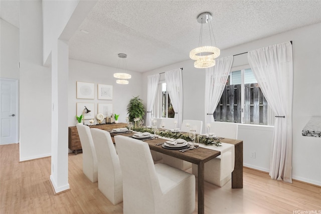 dining area with light wood-style floors, plenty of natural light, a textured ceiling, and a chandelier